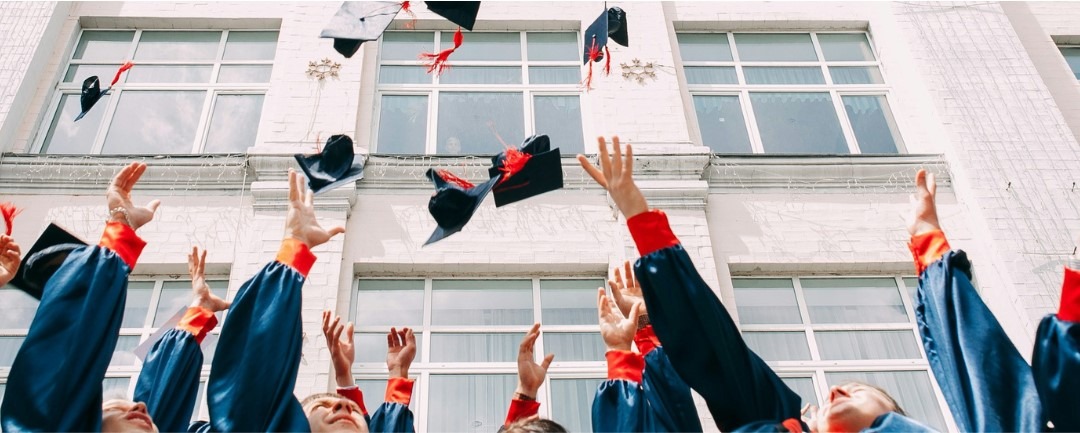 students throwing graduation caps  in the air in front of a white building